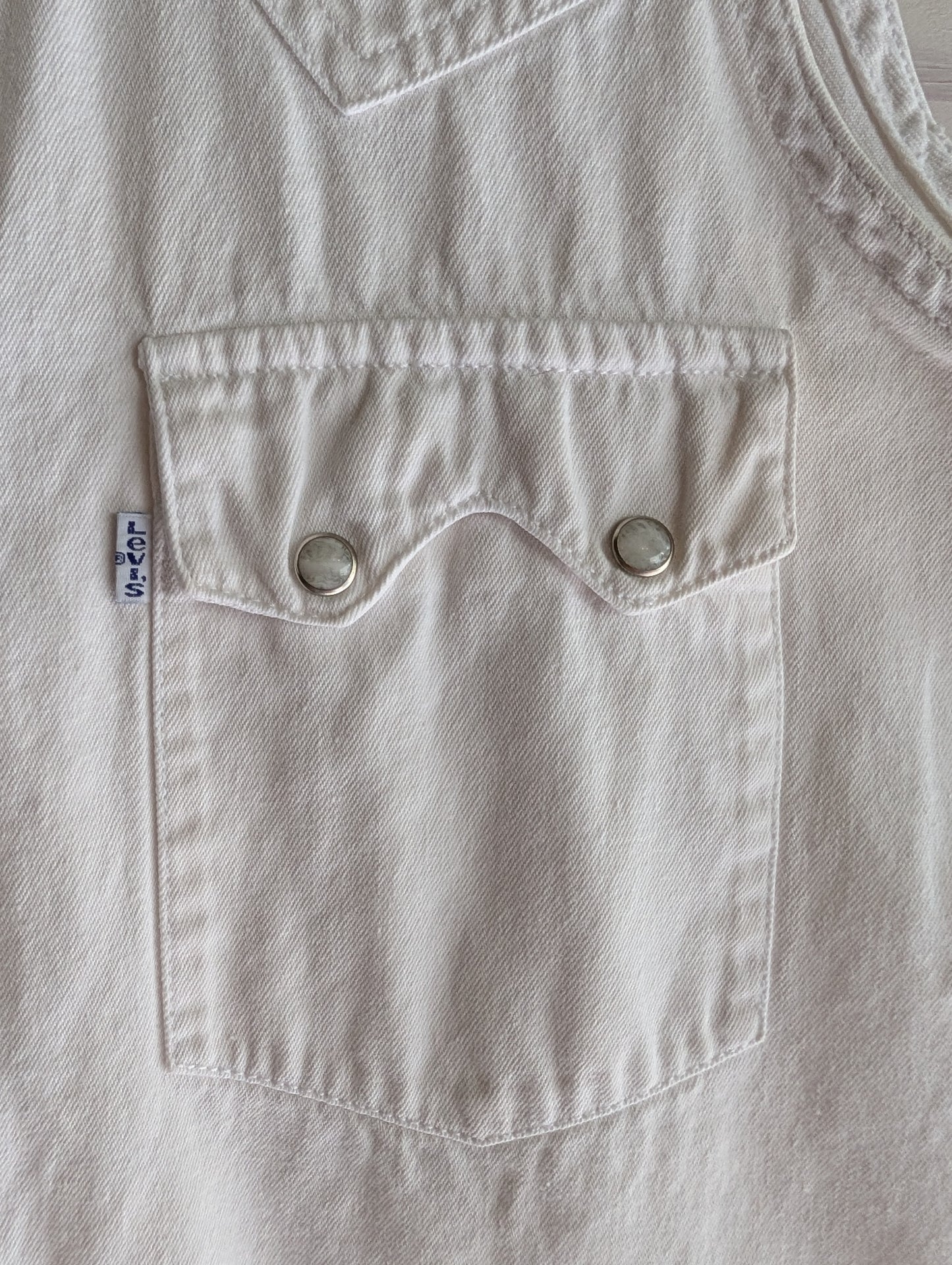 Close-up of a white denim pocket with a white Levi's label with blue writing. Double pearl snaps on pocket. 