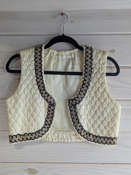 Ivory quilted vest with black and gold sequin trim on a wooden hanger against a wooden background