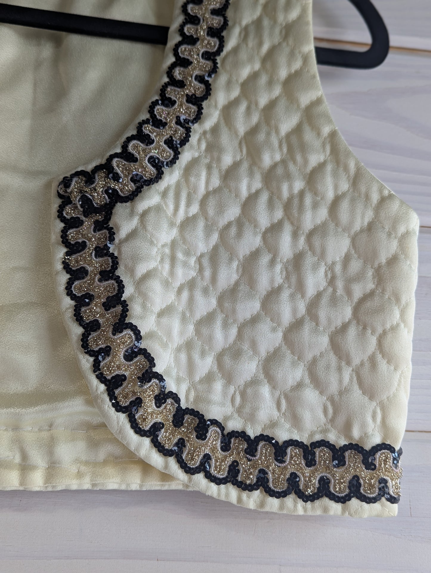 Ivory quilted fabric with black and gold sequin trim on a hanger.
